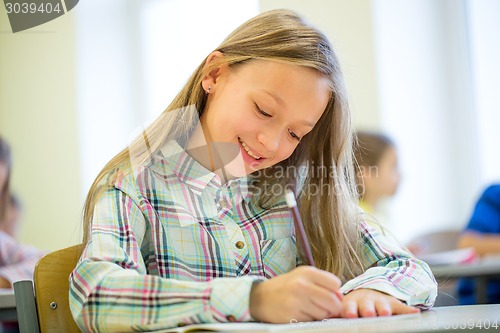 Image of smiling school girl writing test in classroom