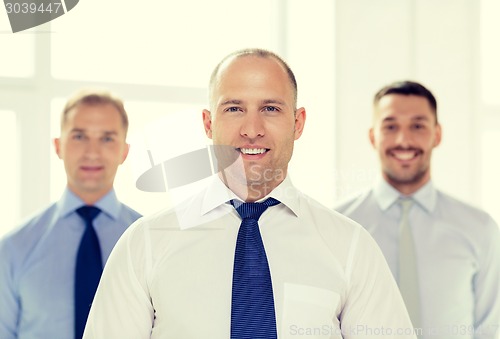 Image of smiling businessman in office with team on back