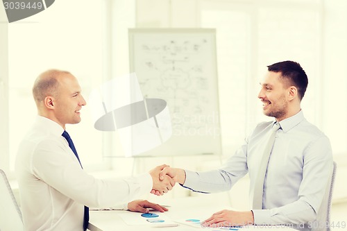 Image of two smiling businessmen shaking hands in office