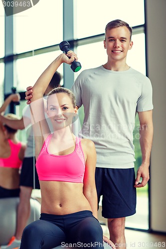 Image of smiling young woman with personal trainer in gym