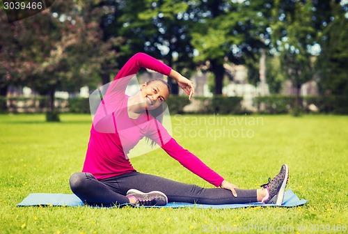Image of smiling woman stretching leg on mat outdoors