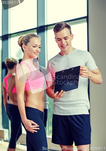 Image of smiling young woman with personal trainer in gym