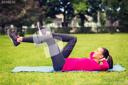 Image of smiling woman doing exercises on mat outdoors