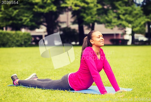 Image of smiling woman stretching on mat outdoors