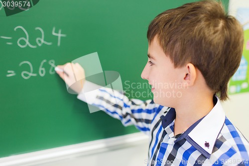 Image of little smiling schoolboy writing on chalk board