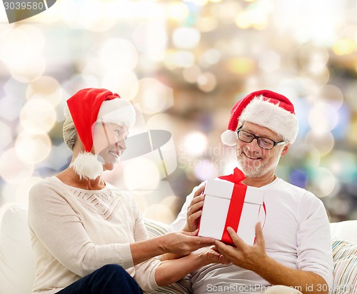 Image of happy senior couple in santa hats with gift box