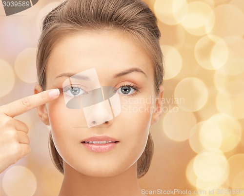 Image of beautiful young woman pointing finger to her eye