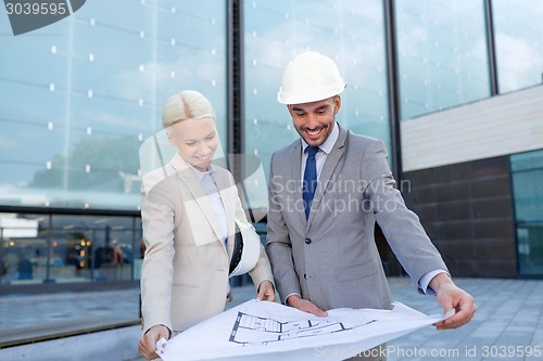 Image of smiling businessmen with blueprint and helmets