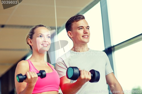 Image of smiling young woman with personal trainer in gym