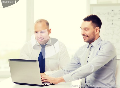 Image of two smiling businessmen with laptop in office