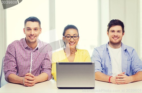 Image of three smiling colleagues with laptop in office