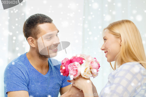 Image of smiling man giving girlfriend flowers at home