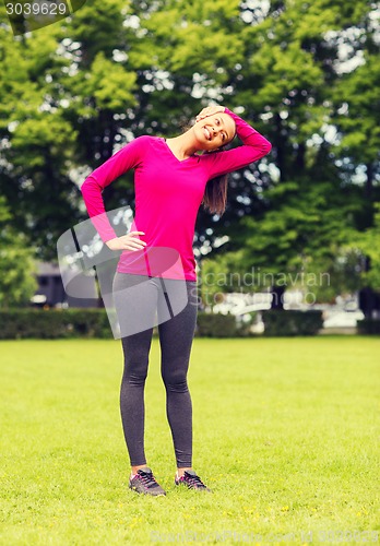 Image of smiling black woman stretching leg outdoors