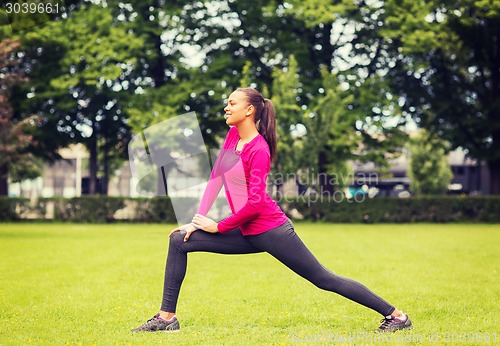 Image of smiling black woman stretching leg outdoors