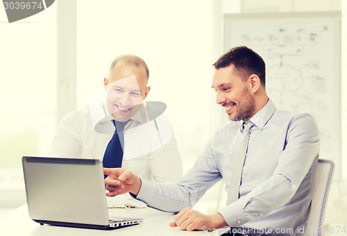 Image of two smiling businessmen with laptop in office