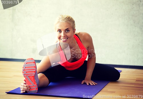 Image of smiling woman doing exercises on mat in gym