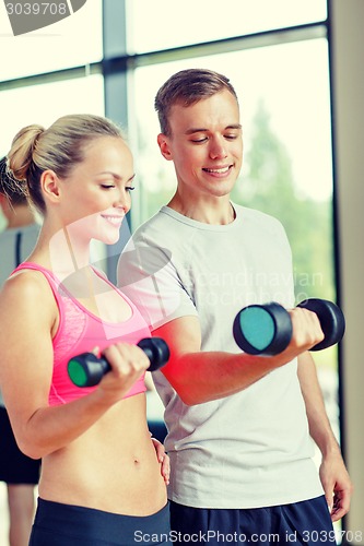 Image of smiling young woman with personal trainer in gym