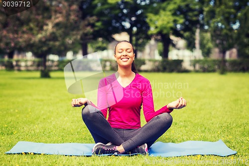 Image of smiling woman meditating on mat outdoors