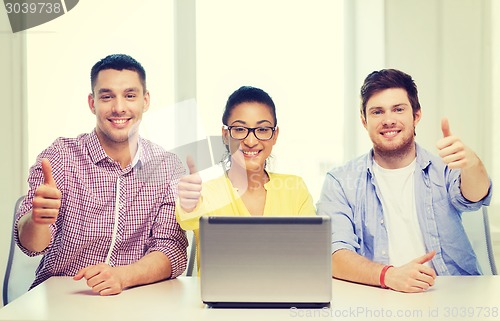 Image of three smiling colleagues with laptop in office