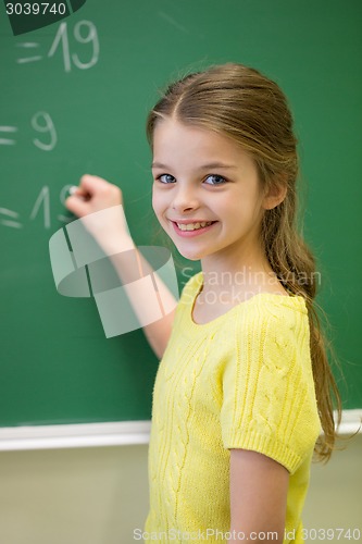 Image of little smiling schoolgirl writing on chalk board