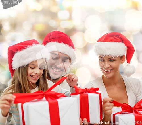 Image of happy family in santa hats sitting with gift boxes