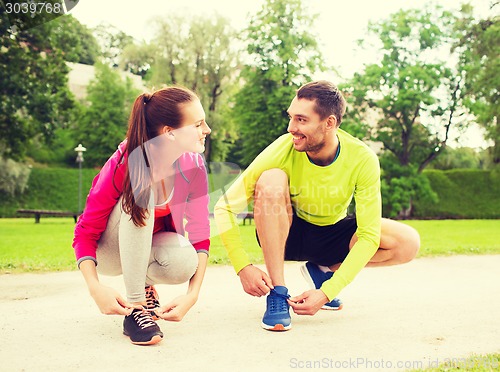 Image of smiling couple tying shoelaces outdoors