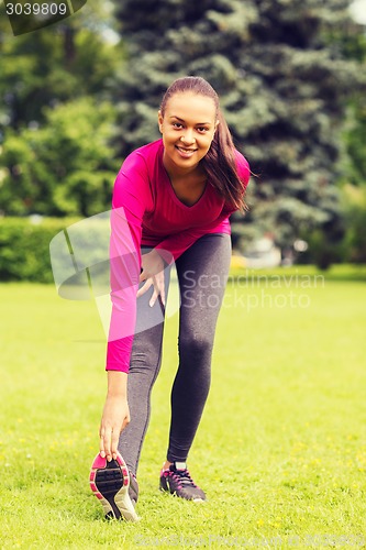 Image of smiling black woman stretching leg outdoors