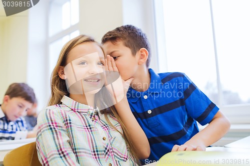 Image of smiling schoolboy whispering to classmate ear