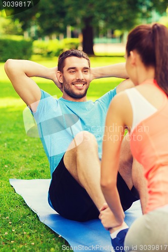 Image of smiling man doing exercises on mat outdoors