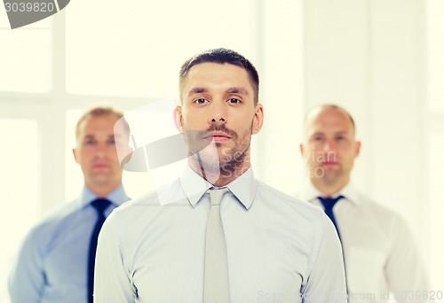 Image of serious businessman in office with team on back