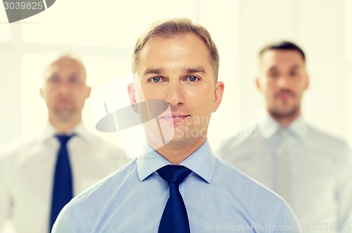 Image of serious businessman in office with team on back