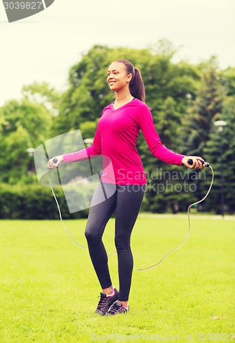 Image of smiling woman exercising with jump-rope outdoors