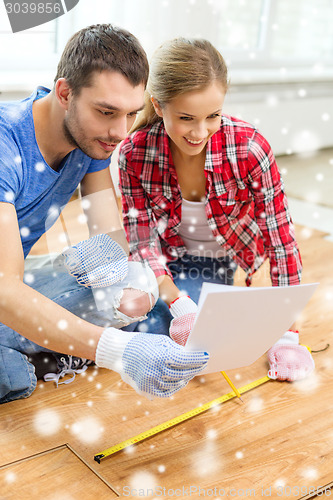 Image of smiling couple measuring wood flooring