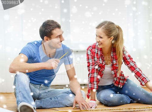 Image of smiling couple measuring wood flooring