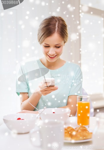 Image of smiling woman with smartphones having breakfast