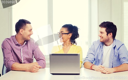 Image of three smiling colleagues with laptop in office