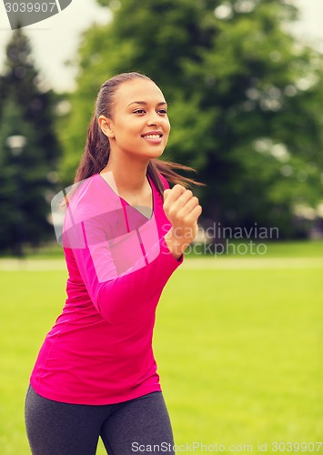 Image of smiling young woman running outdoors