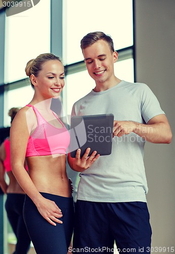 Image of smiling young woman with personal trainer in gym