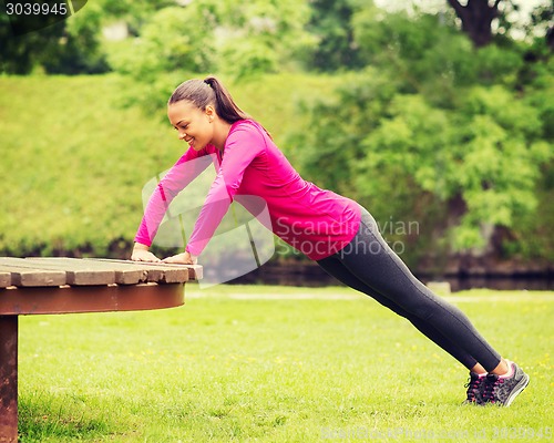 Image of smiling woman doing push-ups on bench outdoors