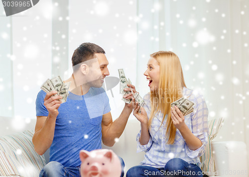 Image of happy couple with money and piggybank at home