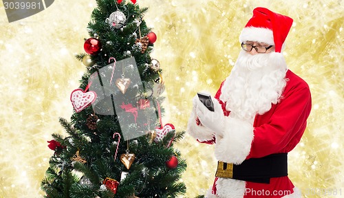 Image of santa claus with smartphone and christmas tree