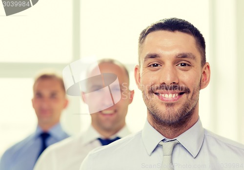 Image of smiling businessman in office with team on back