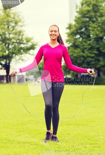 Image of smiling woman exercising with jump-rope outdoors
