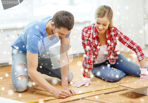 Image of smiling couple measuring wood flooring