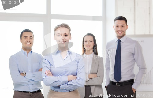 Image of smiling businesswoman in office with team on back