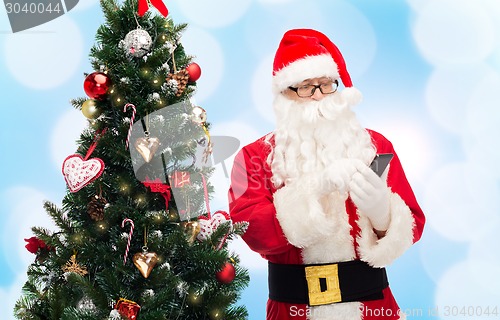 Image of santa claus with smartphone and christmas tree