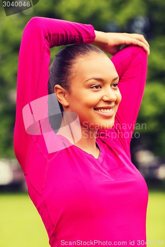 Image of smiling black woman stretching leg outdoors