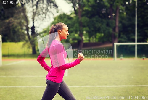 Image of smiling young woman running on track outdoors