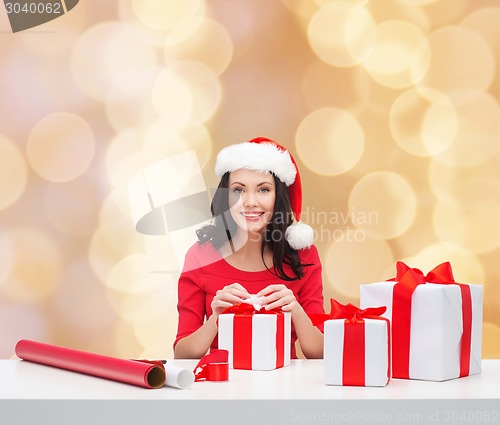 Image of smiling woman in santa helper hat packing gifts