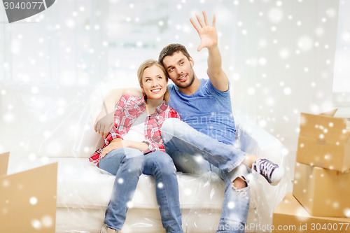 Image of smiling couple relaxing and waving hand at home